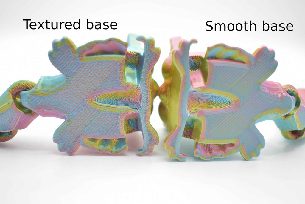 2 Sugarcube gliders, showing the bottom side of the model. 1 has a bumpy texture and the other has a smooth one with text above them on a white background. Text on the left says "Textured base" and the text on the right says "Smooth base"