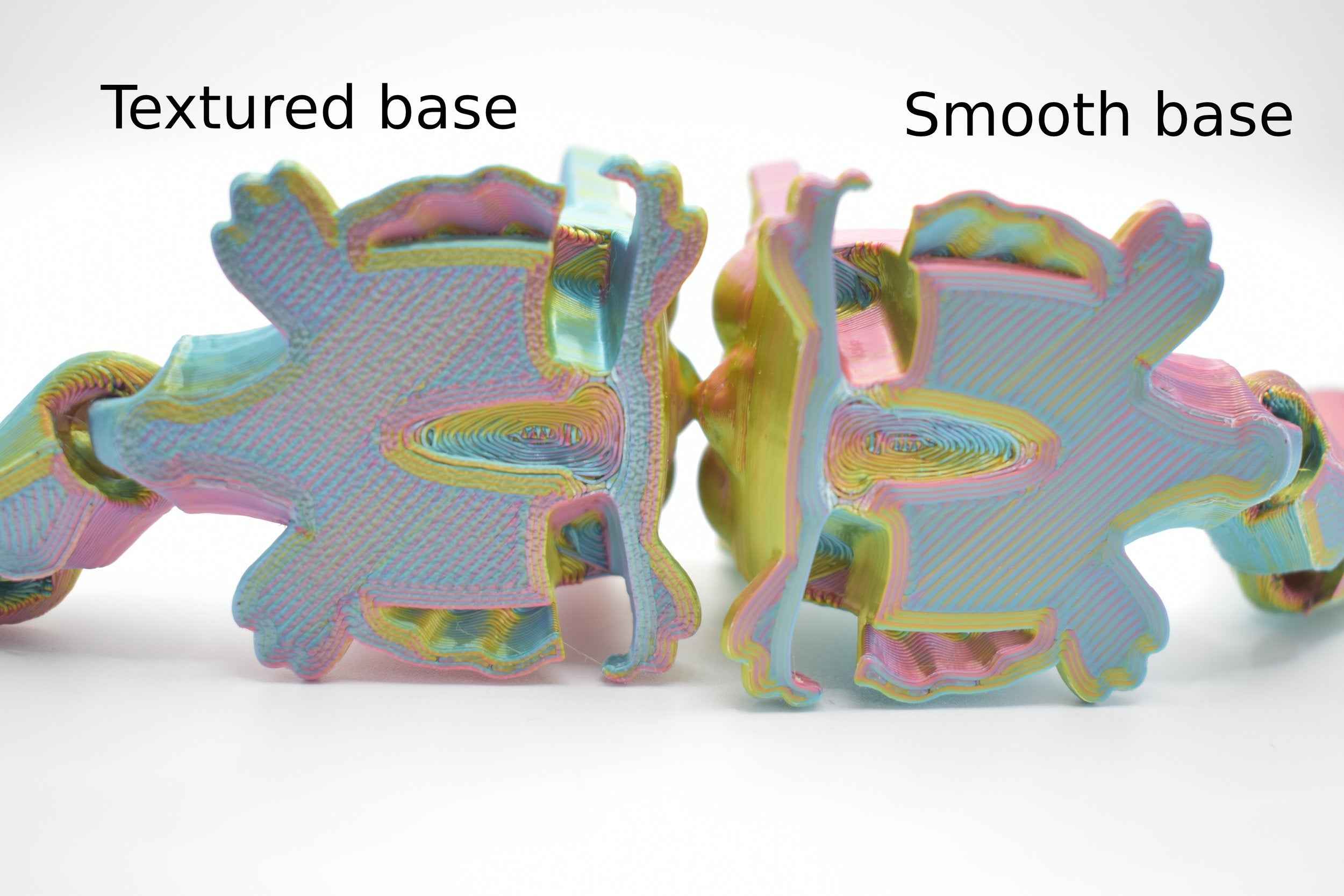 2 Sugarcube gliders, showing the bottom side of the model. 1 has a bumpy texture and the other has a smooth one with text above them on a white background. Text on the left says "Textured base" and the text on the right says "Smooth base"