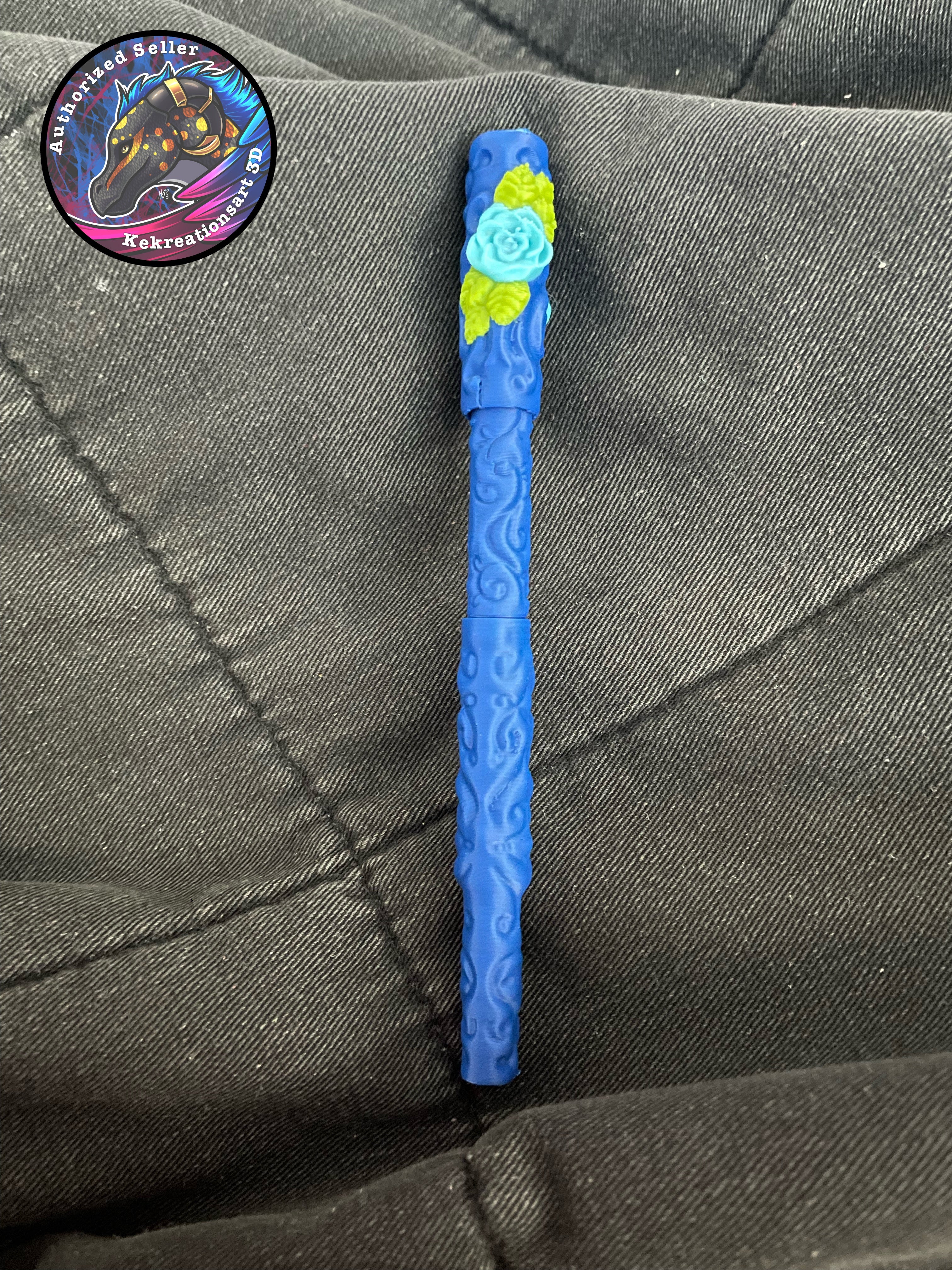 Blue pen with floral design on top against a gray fabric background